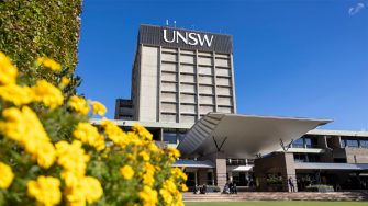 The front of UNSW Main Library building against a clear blue sky, with a portion of the Library lawn and some marigold flowers visible.