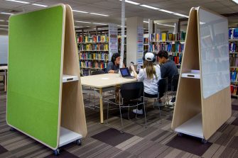 Students sitting at a group study desk next to 2 teepee presentation boards. Book shelving in background.