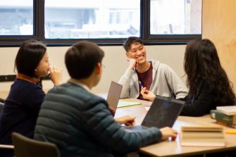 A group of students are in discussion. They are sitting at a large group study desk next to a window, on Level 2 Main Library.