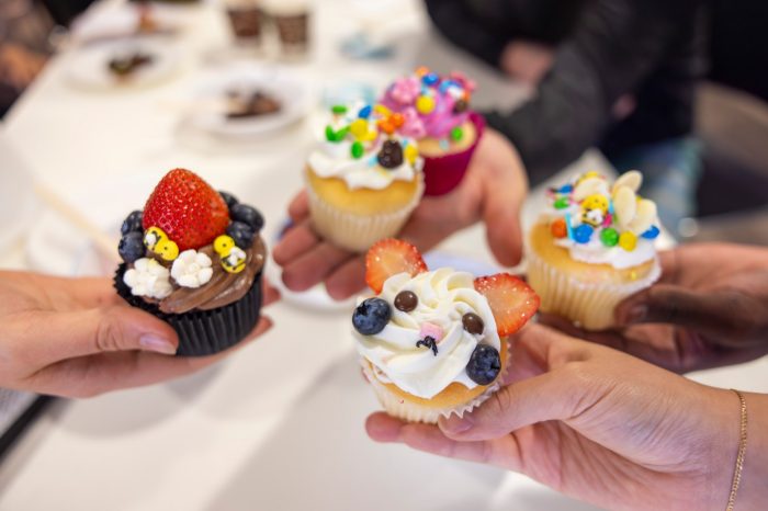 Students holding up their decorated cupcakes at a Library Peer Mentor event. The cupcakes are decorated with colourful icing, berries and candies on top.
