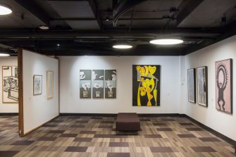 A long shot photo of a gallery space with several artworks hanging on the walls.