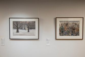 Photo of a gallery wall with two framed painted artworks. The artwork on the left is a wintery scene with two brown tree trunks surrounded by snow. The artwork on the right shows a mass of muted colours with fine, indiscernible detail.