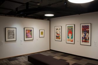 A long shot photo of a gallery space with several framed artworks hanging on the walls.