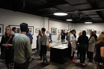 On opening night, a crowd of guests viewing the exhibition and talking to each other.