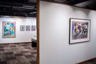 A gallery space with a view across two rooms. Both rooms have colourful abstract paintings hanging from the wall. 