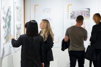 A photo of four people viewing wall mounted artworks. Two of them gesture towards the works with their hands. 