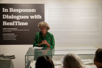 Professor Sarah Miller speaking in front of exhibition installation title text