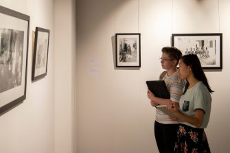 Two people look at a series of framed photographs hanging on a wall