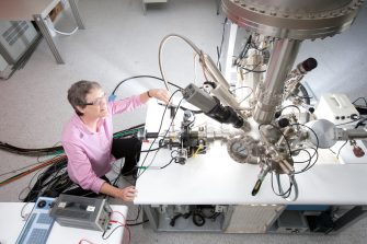 A woman wearing glasses and a pink shirt adjust gleaming metal technical equipment