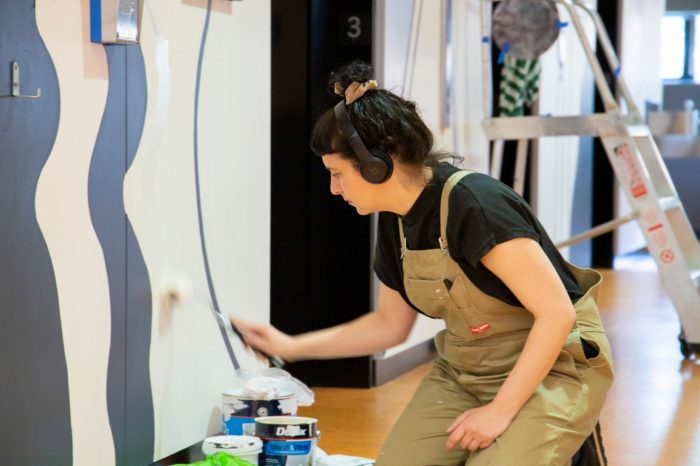 Lisa Summut painting mural on south wall near first lift of lift foyer 