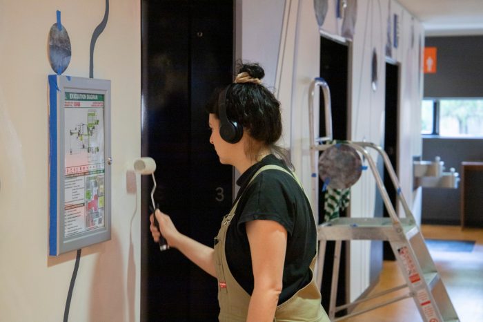 Lisa Summut painting mural on south wall near first lift of lift foyer 