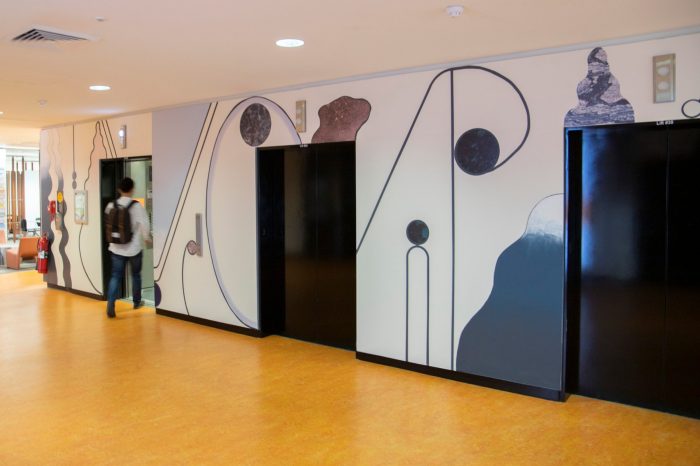 An abstract mural surrounding elevator lifts comprised of curving shapes, pale shades of purple, cream, blue, and textured wall decals