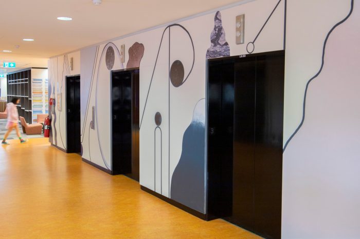 An abstract mural surrounding elevator lifts comprised of curving shapes, pale shades of purple, cream, blue, and textured wall decals