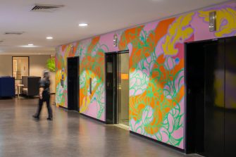 A person walking away from a multicoloured abstract mural surrounding elevator lifts