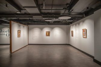 A dimly lit room with text and small colourful paintings on the walls, black ceiling, grey floor.