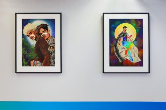 Installation view of two framed prints. The work of the left features two young men embracing against the night sky. The work on the right features a young man with multicoloured body, wearing a fur cape, set against a bright yellow full moon.