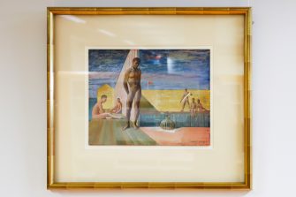 Installation view of a gold framed painting, portraying nude figures lounging by an outdoor bathhouse against a blue, clouded sky.