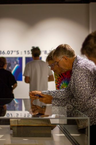 Photo of two people leaning over a glass display cabinet, pointing a large book encased within.