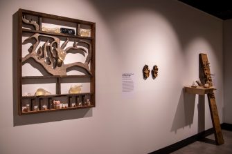 Wooden sculptures bearing organic forms like mushrooms and fungi hang on the wall. A pair of hands made of timber hang in the centre.