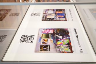 A side-on photo of two posters in a glass display unit. The posters show colour, abstract images, with the title "Framework", and a QR code. 