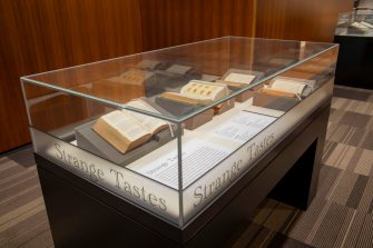 A photograph of a display case featuring four books propped open to display recipes and food illustrations