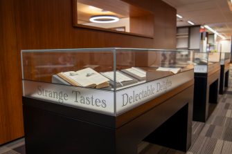 A photograph of a display case featuring four books propped open to display recipes and food illustrations
