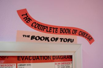 A close up of a purple wall with an illustration of two books. Their titles read, "The Complete Book of Cheese" and "The Book of Tofu".