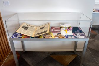 A glass display cabinet containing two older-style magazines propped up against a colourful backdrop