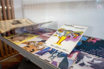 A side-on photo of a glass display cabinet containing two magazines propped up against a colourful backdrop. The magazine closest to the camera shows a flowery illustration of a uterus. 