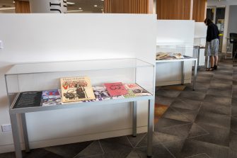 A library area with three glass cabinets displaying colourful magazines. A person is peering into one of the dispays.