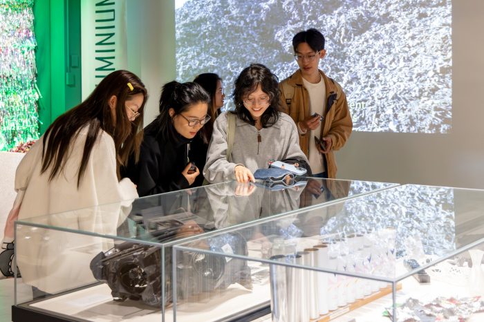 Three university students gather around a glass display case in an exhibition space. They are smiling at pointing at the content inside. 