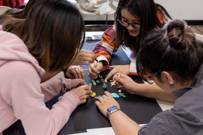 People gather around a table, with small objects and white pencils in the act of drawing.