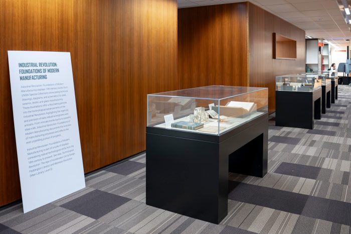 A line of four glass display cases lined up along a library walkway.
