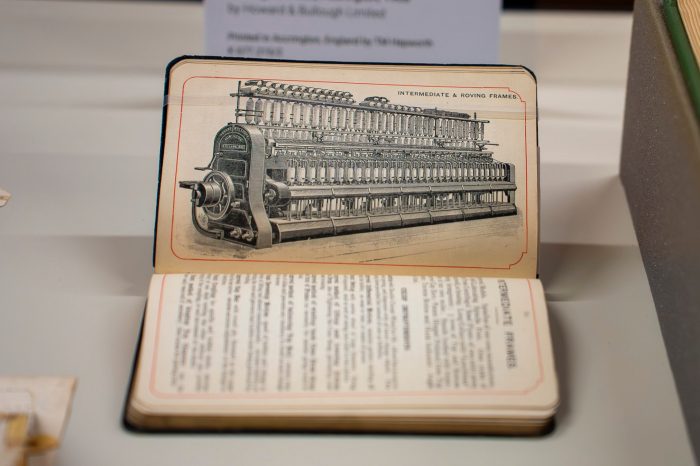 Close-up of an old book, opened to a page showing a black and white illustration of a elaborate 19th Century textile machine