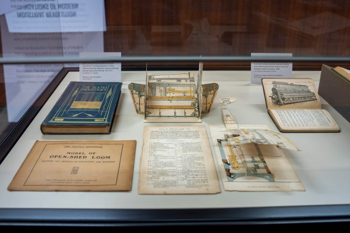 A glass display case containing several old books. Two of the books are opened on decorative pop-up pages, showing mechanical drawings.