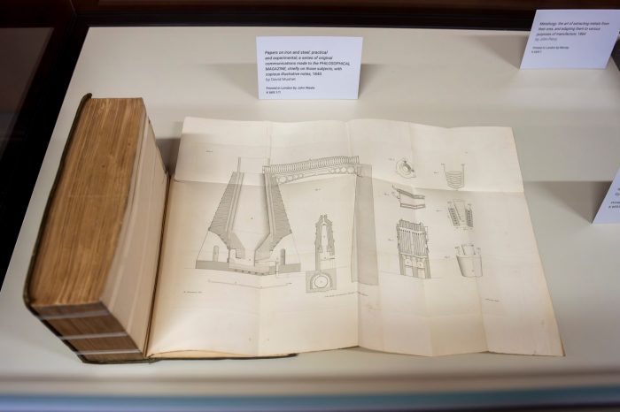 An old book opened to a folded-out page showing a finely detailed drawing of mechanical parts