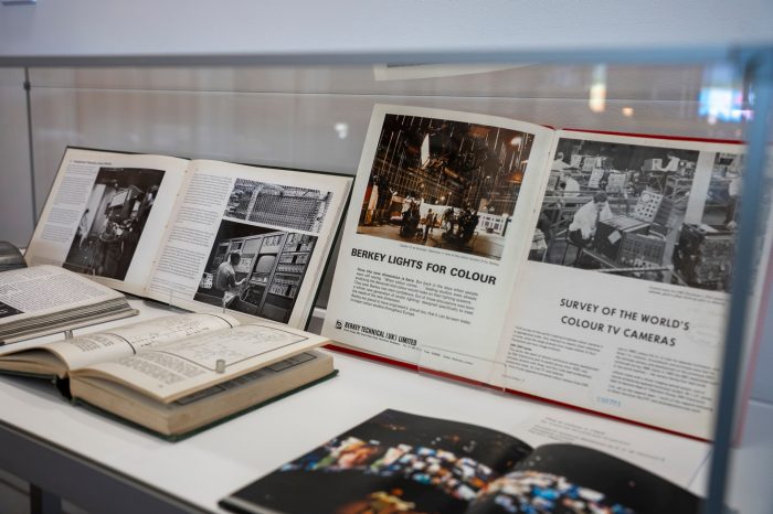 A glass display case containing several booked opened to pages showing images of 1950s computers and television broadcast studios