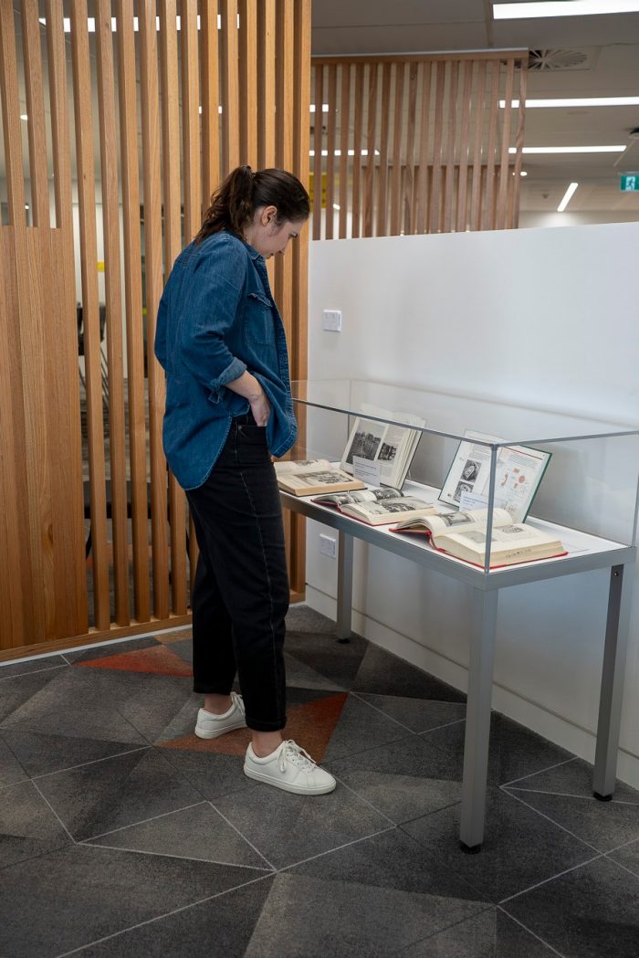 A woman in a blue shirt looks into a glass display case containing several books