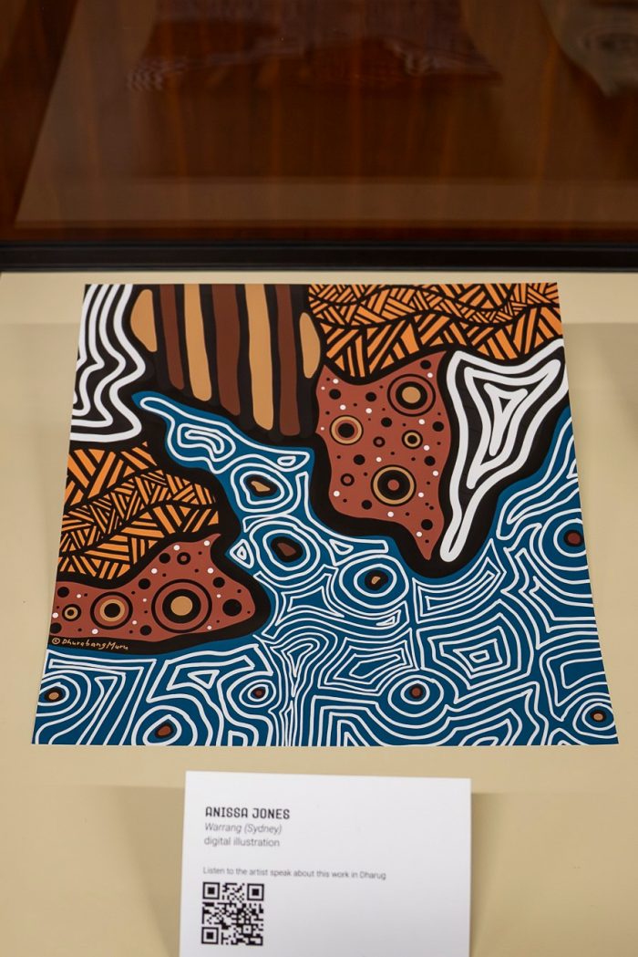 View of a printed digital artwork inside a display case. The artwork shows an abstracted coastline with brown lines and circles as the land, and patterned white and blue lines as the sea.  