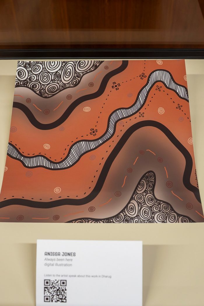 A view of an illustrated digital print in a glass display case. The illustration is an abstracted desert landscape with tones of brown and orange, with striking dark lines, symbols, and patterns. 