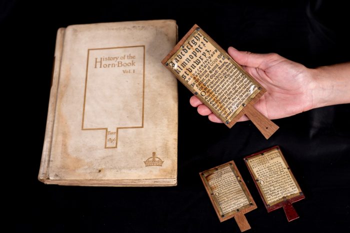 A visibly-aged book, History of the Horn-Book, sits beside three actual horn-books, one held by a person's hand.