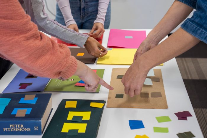 Hands move small coloured squares of paper on larger sheets of coloured paper.