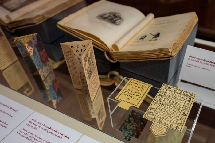 A display case containing two cardboard horn books surrounded by books and written labels.