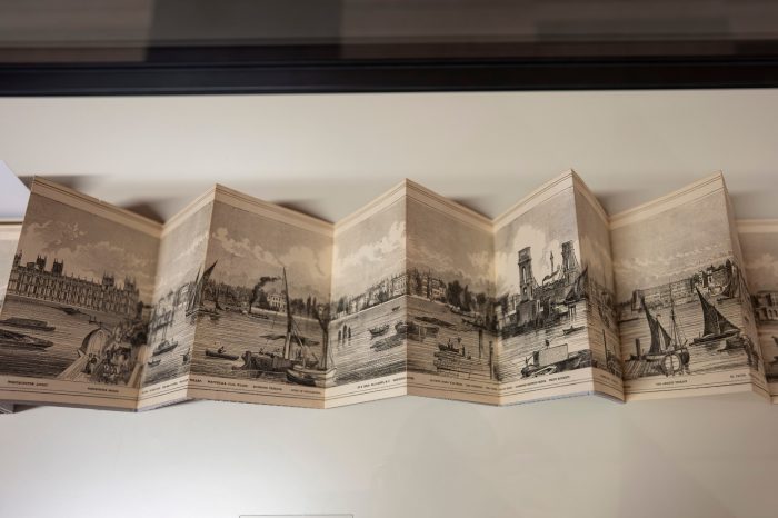 An outstretched concertina book opened to display a black and white panoramic photo of a harbour.  