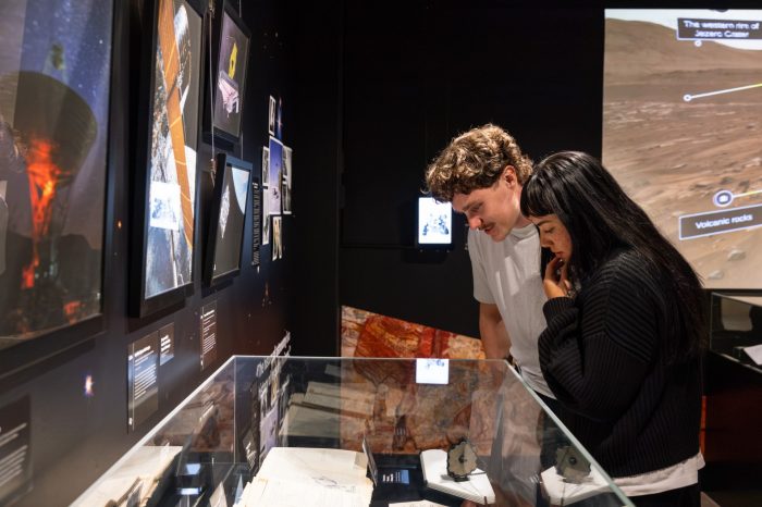 Two visitors leaning over a glass display case to examine historical manuscripts and a small model of a telescope.