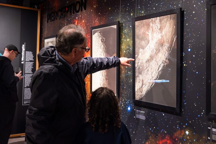 A visitor points to a framed, detailed photograph of the moon's surface while talking to a child.