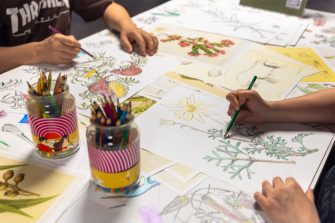 Two people sitting at a table using pencils to colour in a paper tablecloth