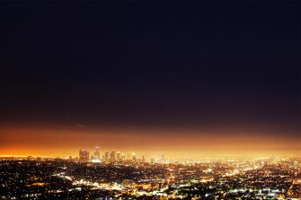 A landscape view of a large city at nighttime, as seen from far away. The city lights create a orange glow against the dark, starless sky