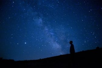 A person silhouetted against a deep blue starry night