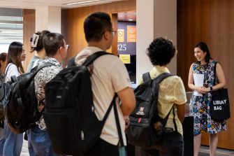 A smiling woman stands in front of a group of university students in an exhibition area